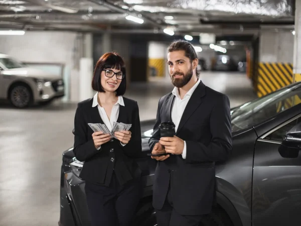 Caucasian businessman and businesswoman in formal attire counting money in car parking lot. They exhibit confidence and success in business environment.